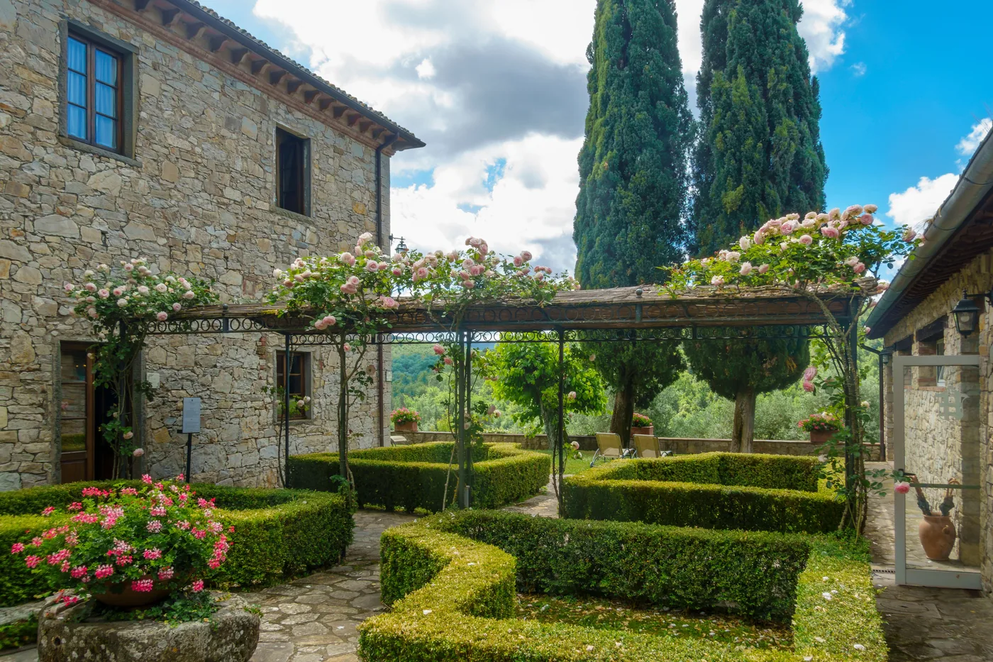 A stone villa garden with clipped hedging, cypress and roses